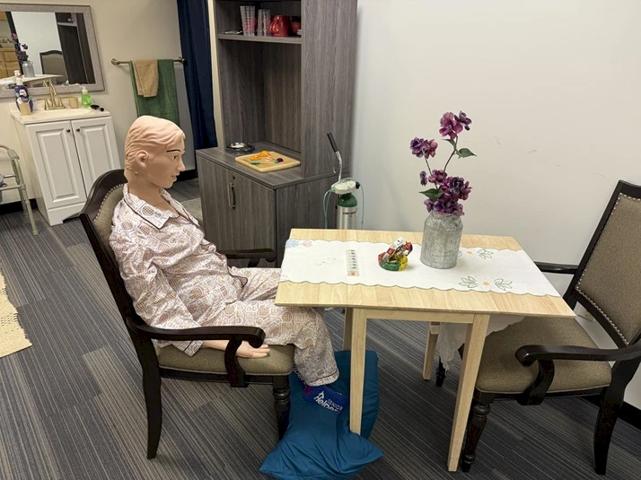 “Darla” the Manikin sits at the table at the Senior Helpers Portland West Center of Excellence kitchen simulation. Caregivers are taught how to safely help seniors with activities of daily living.